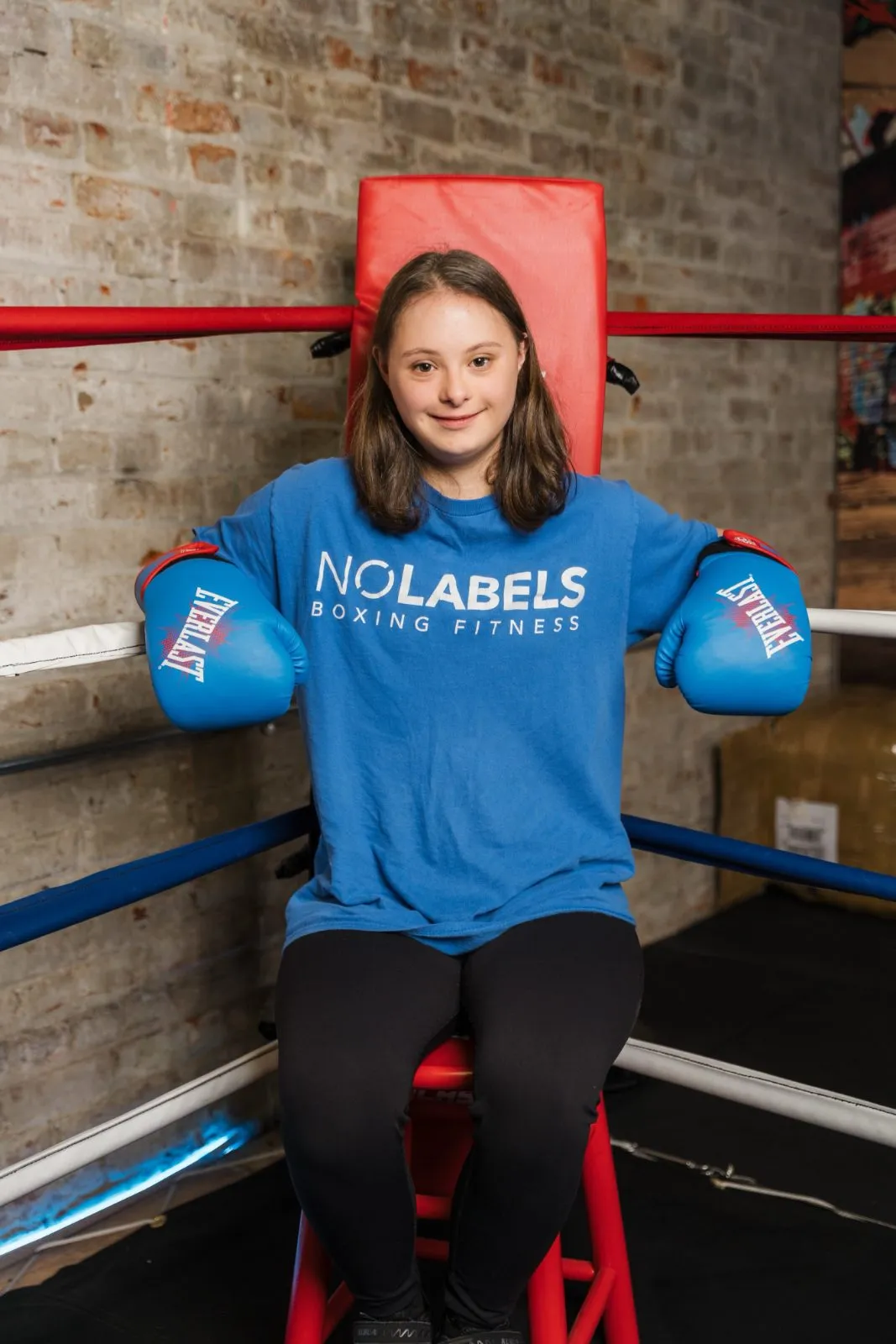 A young athlete in No Labels gloves sitting in the ring corner