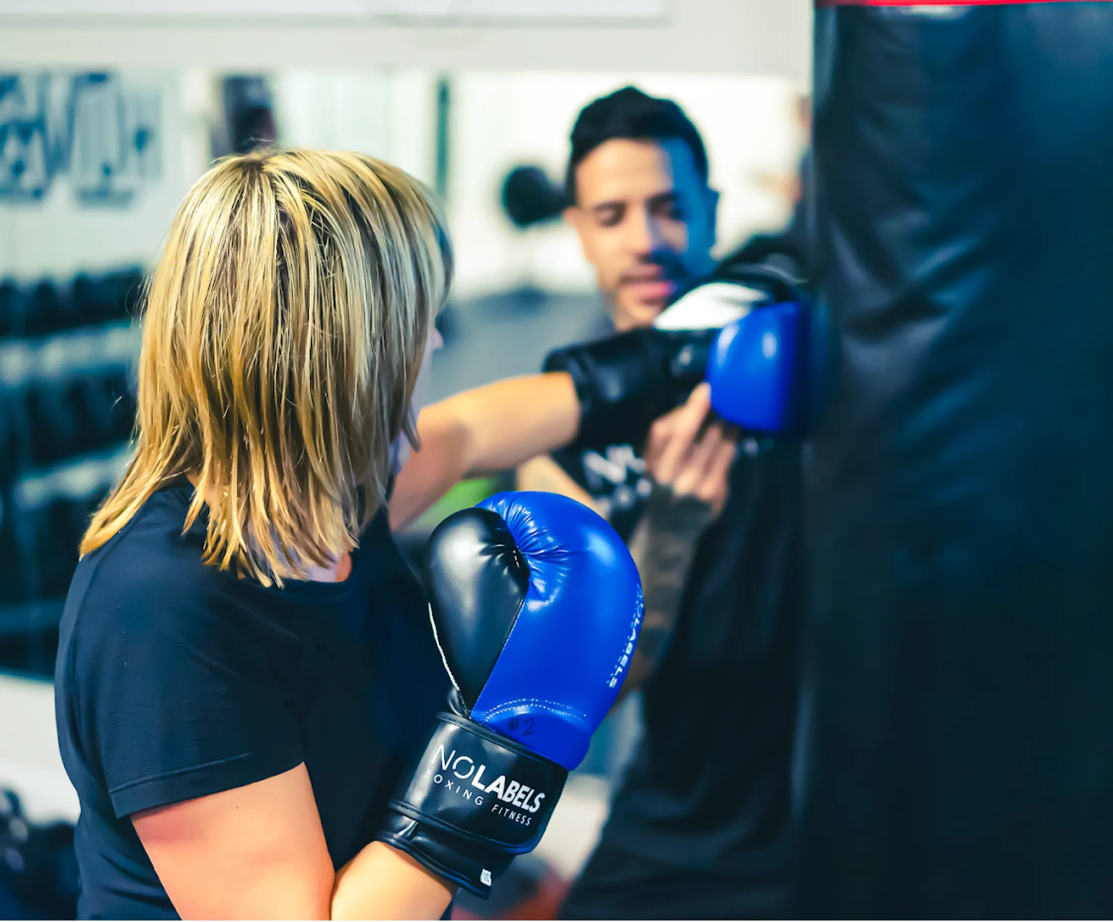A member throwing a punch at the heavy bag while a coach holds it